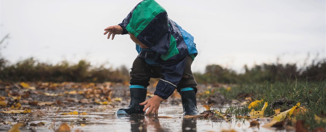 kleines Kind in Regenkleidung spielt im Regen