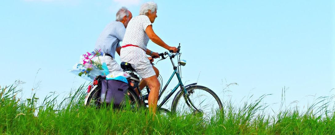 zwei ältere Personen fahren Fahrrad über eine Wiese